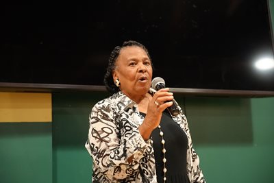 Gladys Muhammad stands with a microphone in hand.